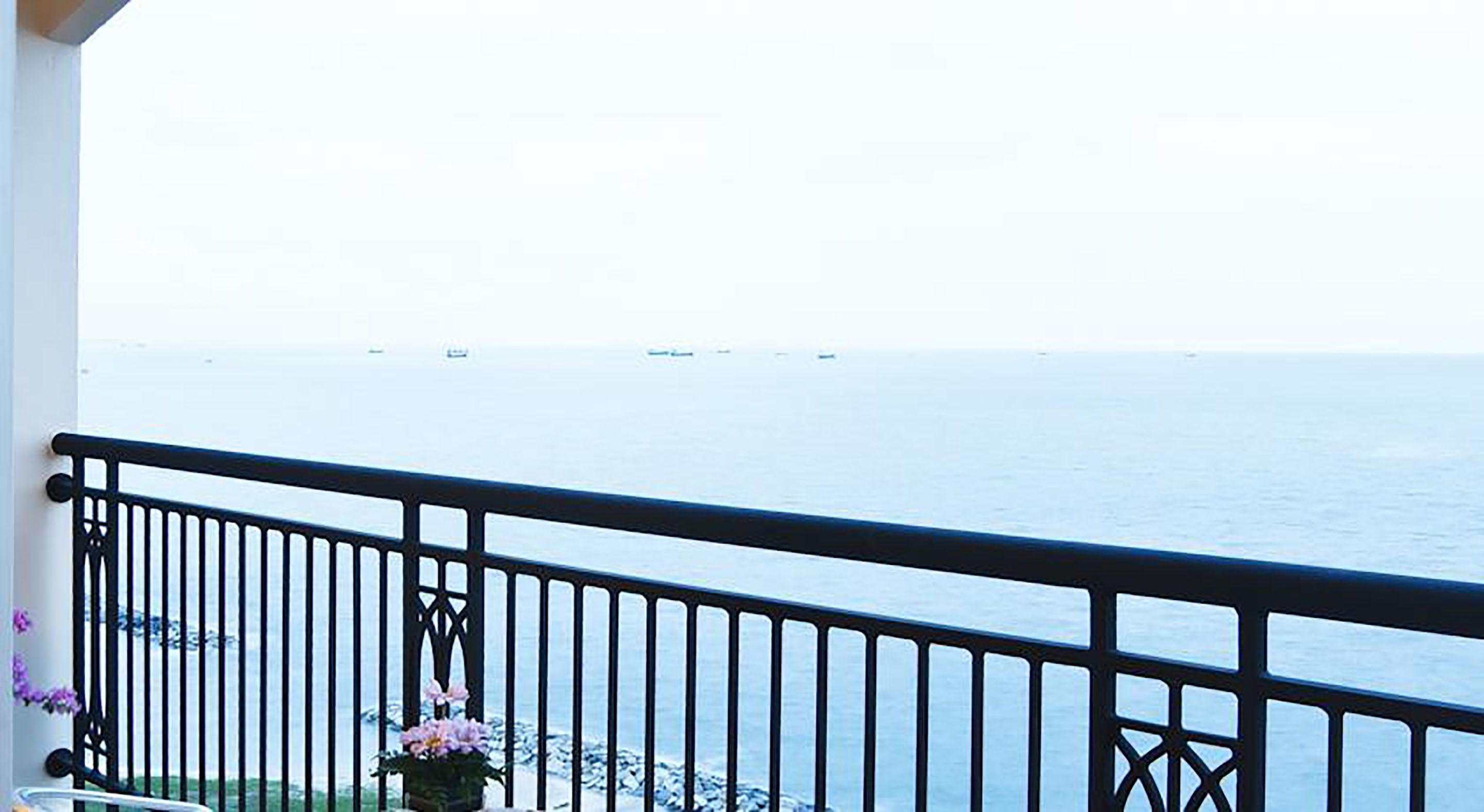A balcony with a black metal railing overlooking a calm sea.