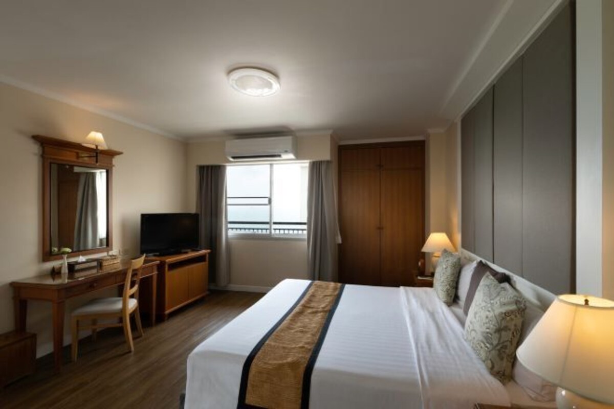 A hotel room with a bed, desk, TV, and a window with curtains.
