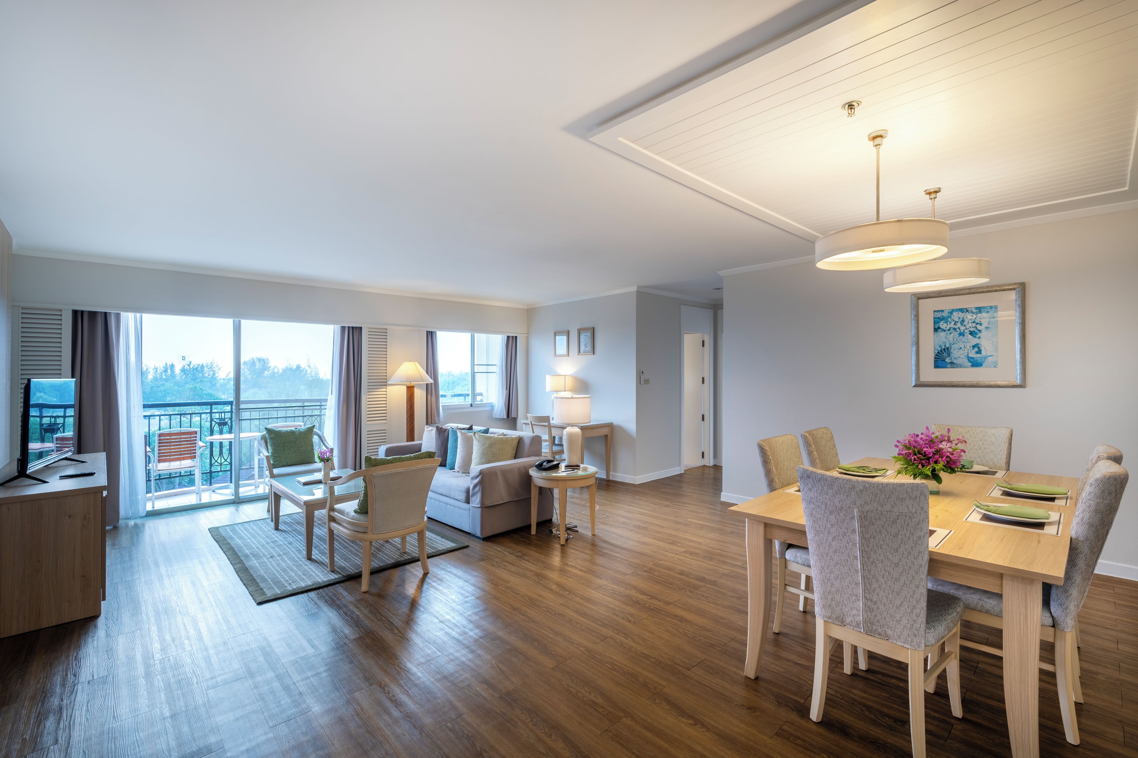 A spacious living area with a dining table, chairs, and a balcony with outdoor furniture.