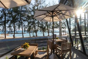 An outdoor seating area with tables and chairs, overlooking a body of water and trees.