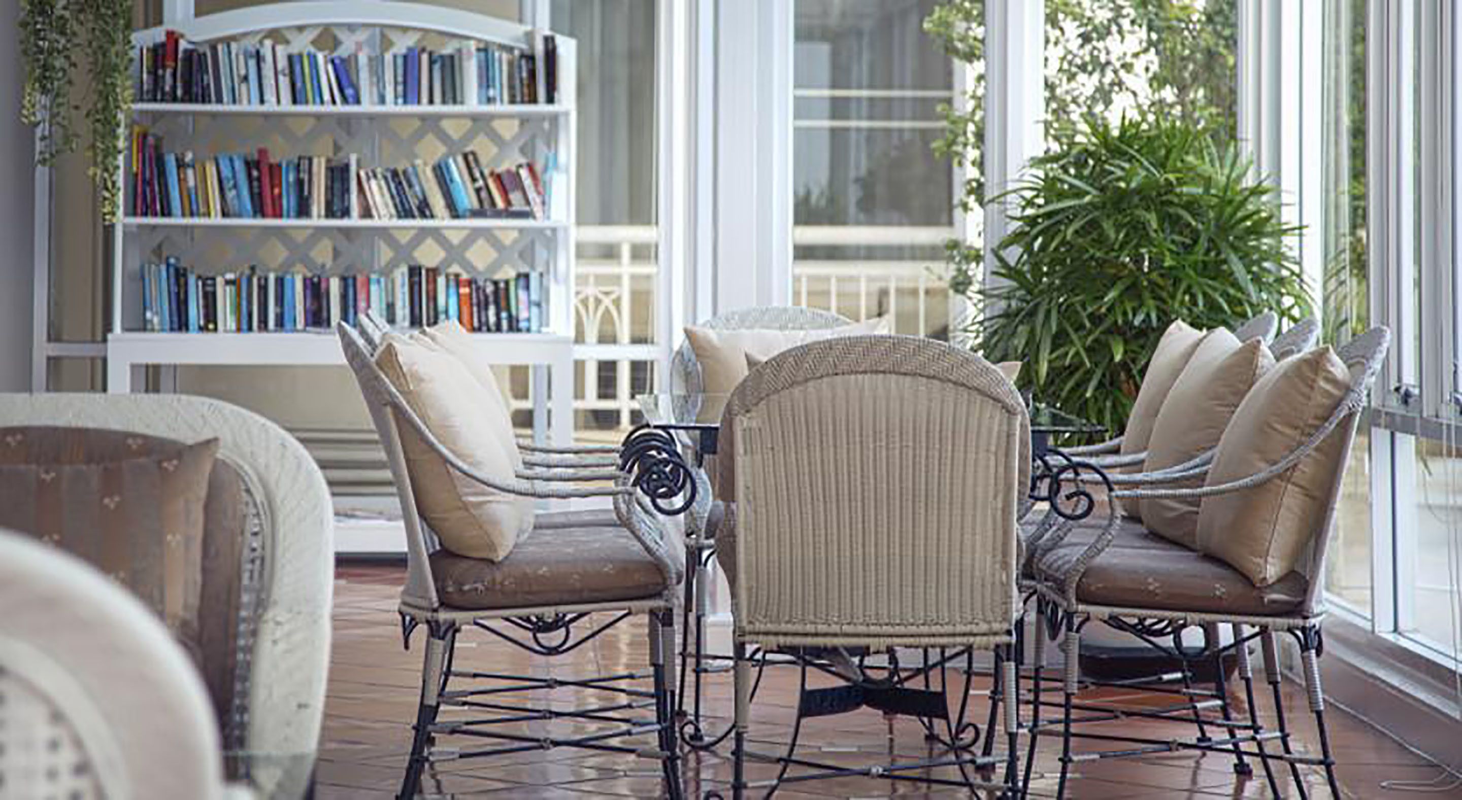 A sunlit reading area with wicker chairs and a bookshelf filled with books.