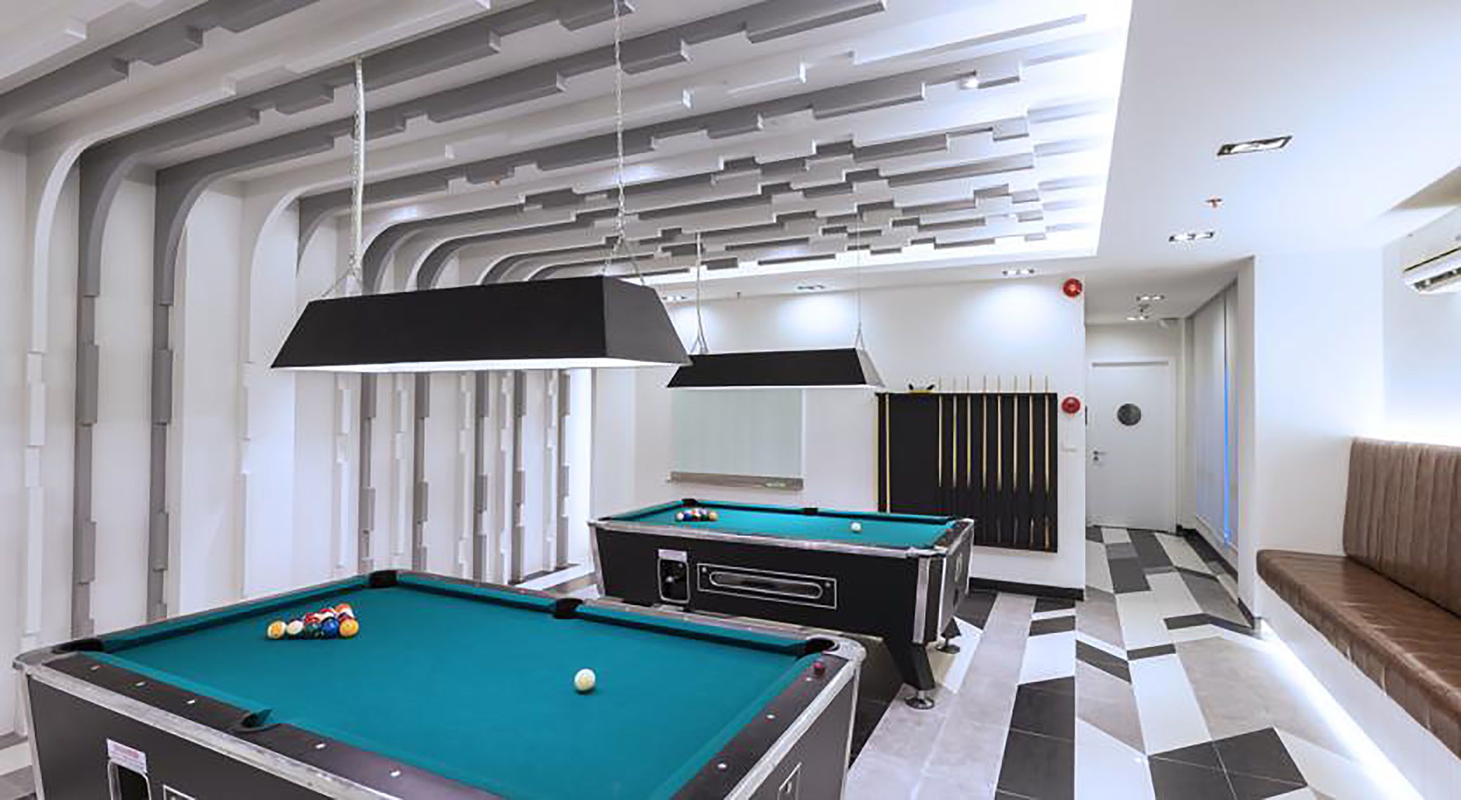 A modern pool table with a green felt surface, a second table in the background, and a checkered floor pattern.