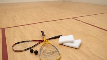 En squashhall med trägolv, ett tennisracket, ett squashracket och två svarta bollar.