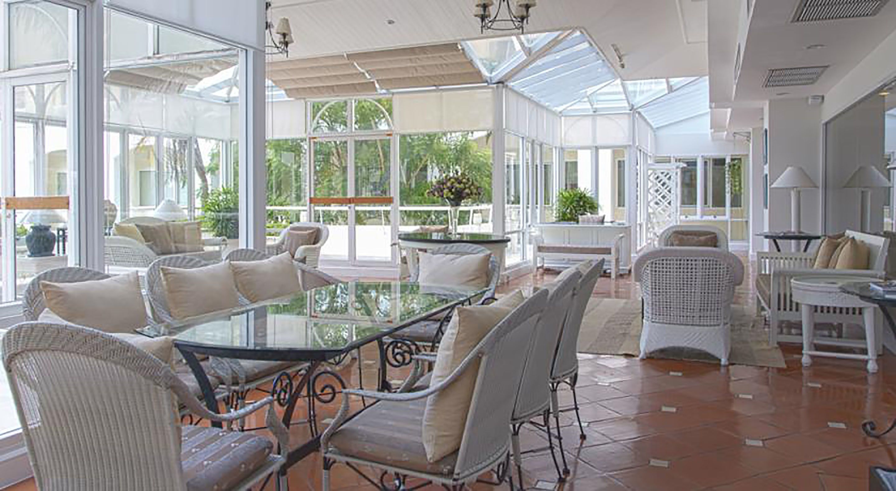 A spacious patio with a glass-top table surrounded by wicker chairs, white sofas, and a white dining table.