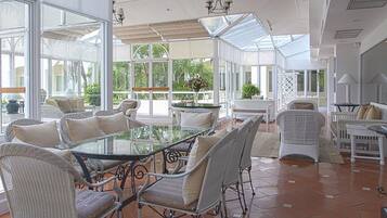 A spacious patio with a glass-top table surrounded by wicker chairs, white sofas, and a white dining table.