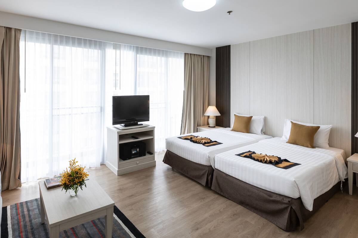 A hotel room with two beds, a TV on a stand, a lamp, and a coffee table with a vase.