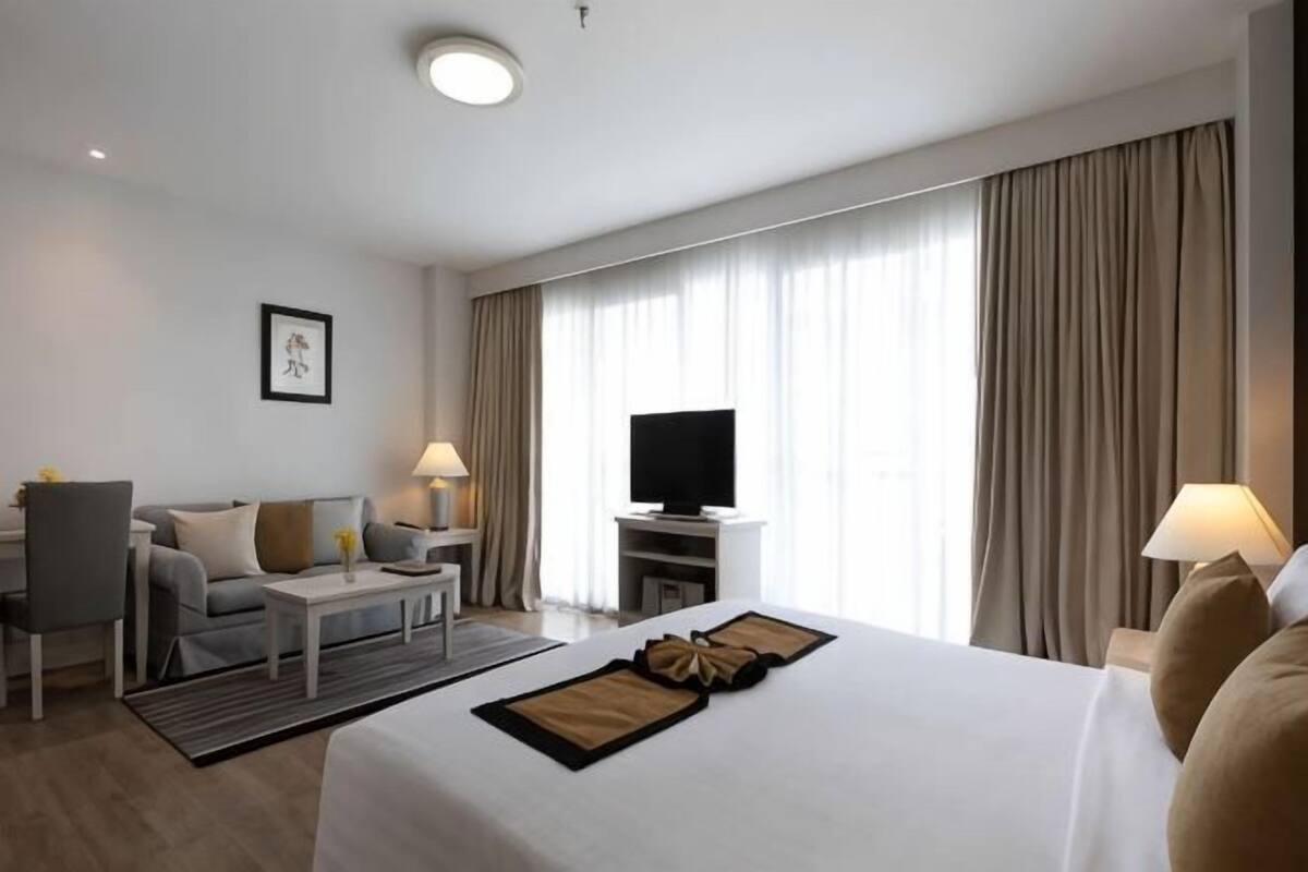 A hotel room with a bed, a desk, a chair, a TV, and a window with curtains.