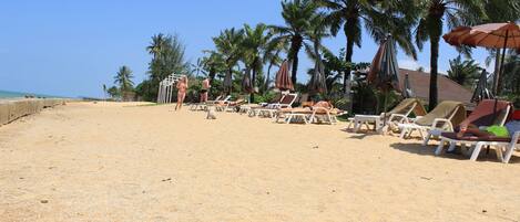 A beach with sun loungers, umbrellas, and palm trees.