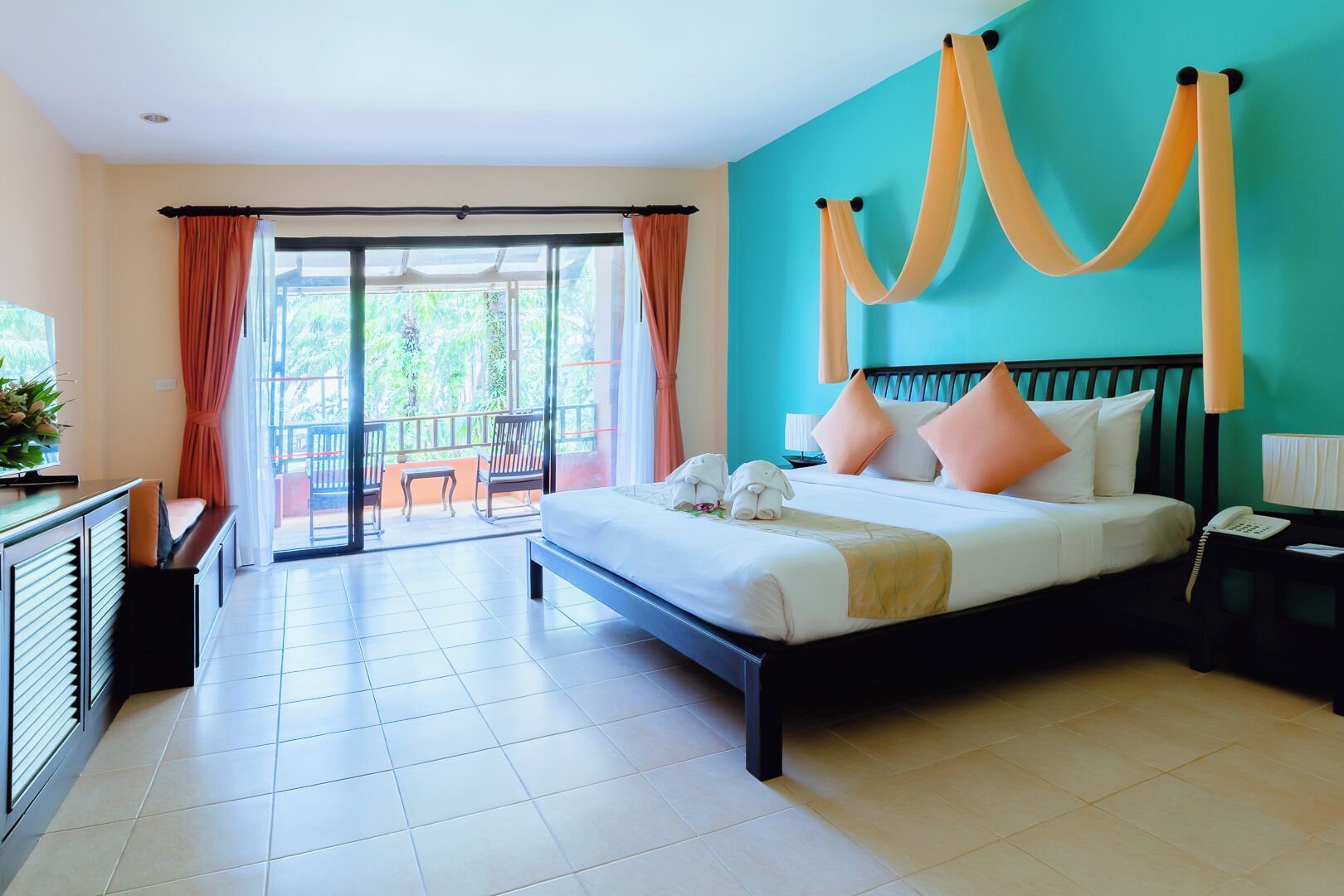 Een hotelkamer met een bed, bureau, stoel en een balkon met uitzicht op groen.