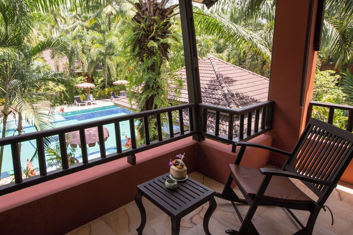 A balcony with a view of a swimming pool, surrounded by lush greenery.