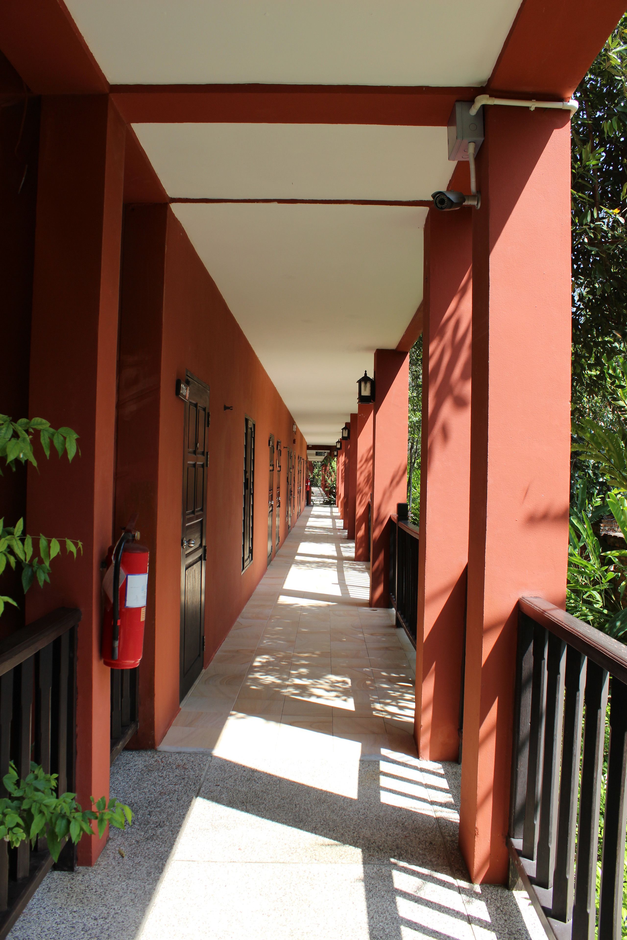 A corridor with red walls, a fire extinguisher, and a metal railing.