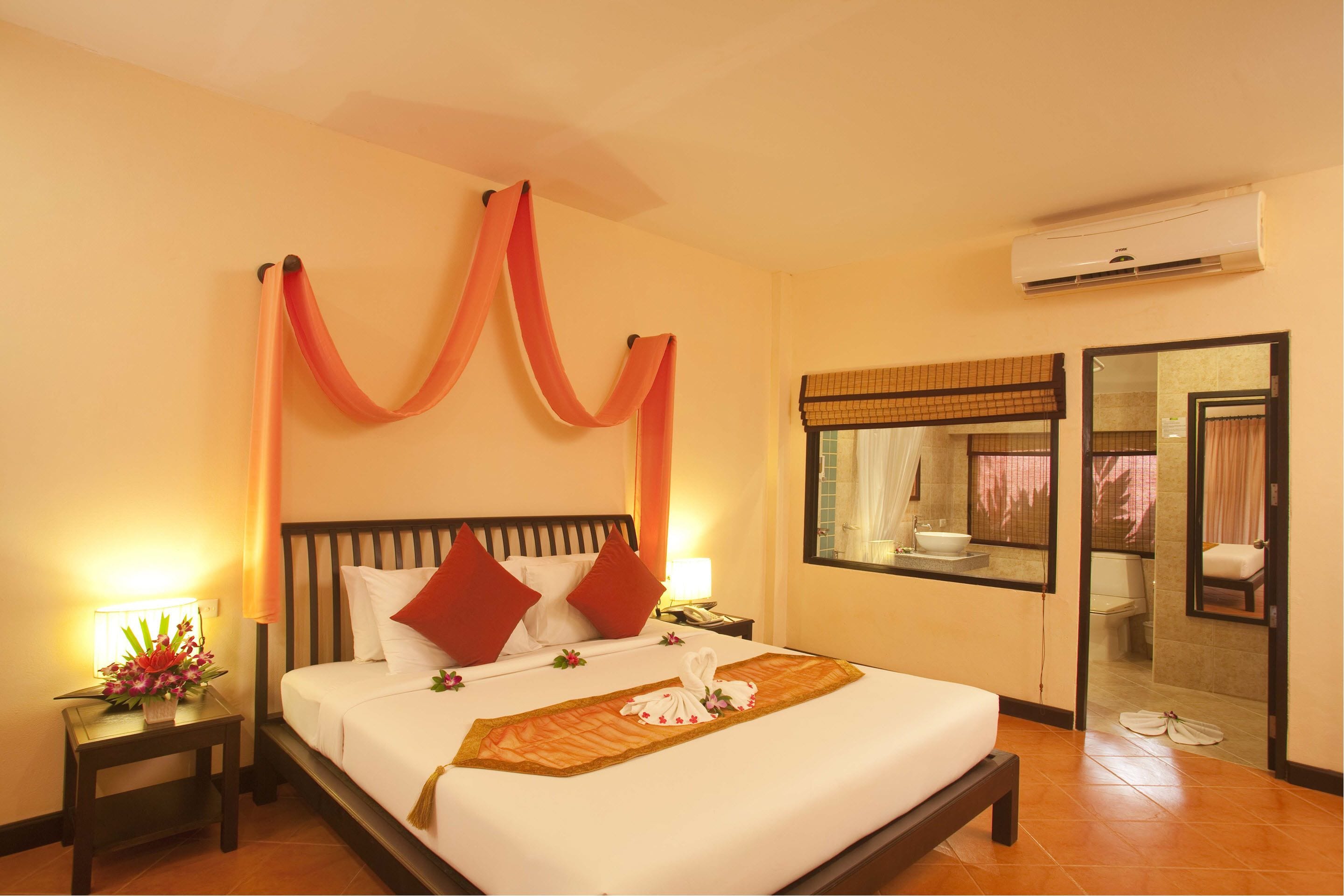 A hotel room with a bed, a nightstand, a mirror, an air conditioning unit, and a bathroom visible through an open door.