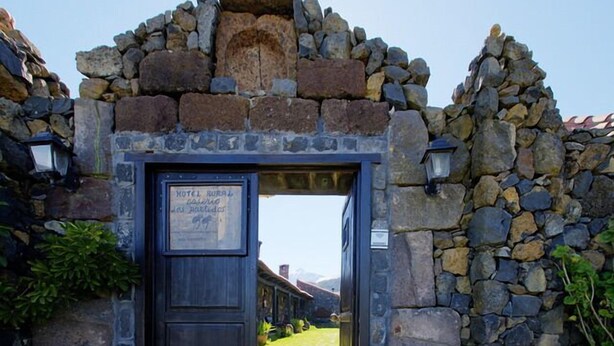 Un arco de piedra rústico que da paso a la entrada de un hotel, con un cartel que indica que es un hotel rural.
