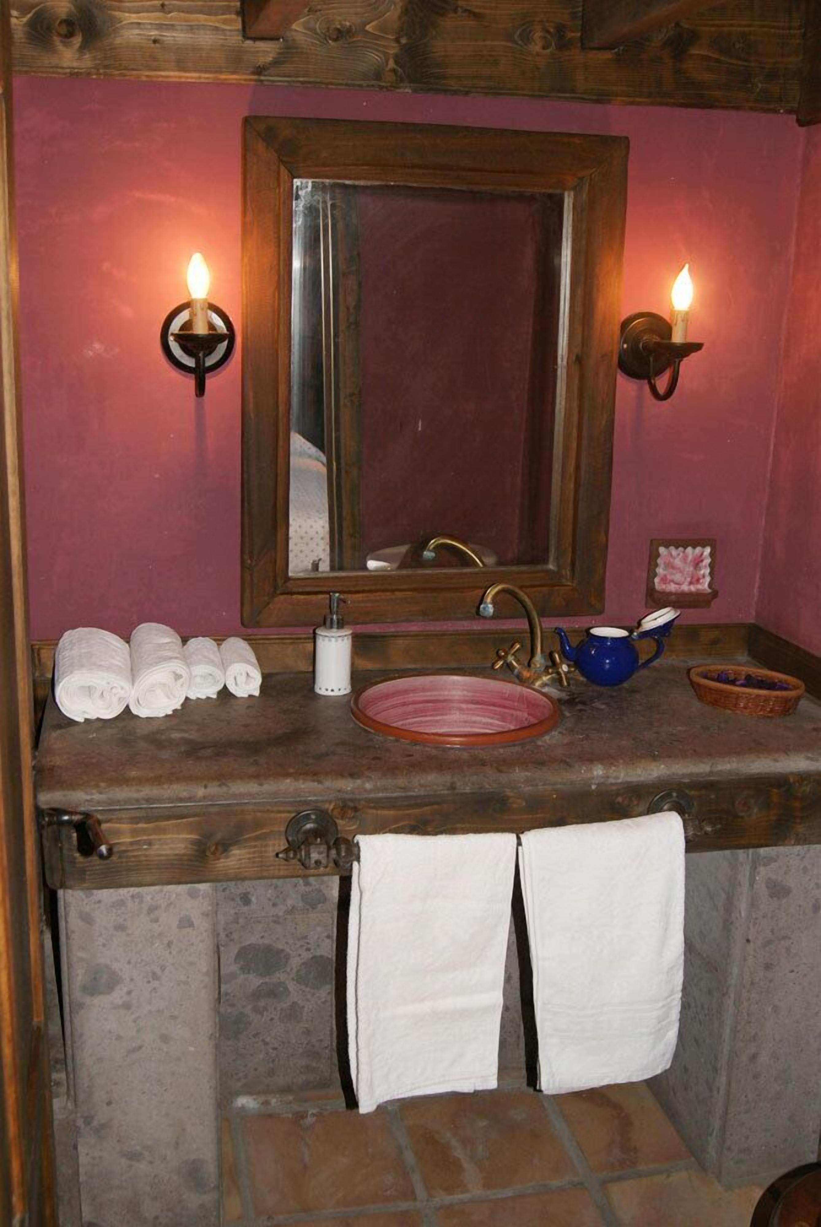 A bathroom with a wooden vanity, a pink sink, and two wall-mounted candles.