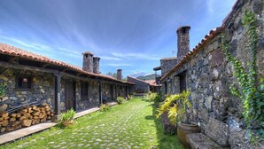 Un patio con edificios de piedra, un camino adoquinado y montañas al fondo.