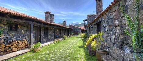 A courtyard with stone buildings, a cobblestone path, and a mountain backdrop.