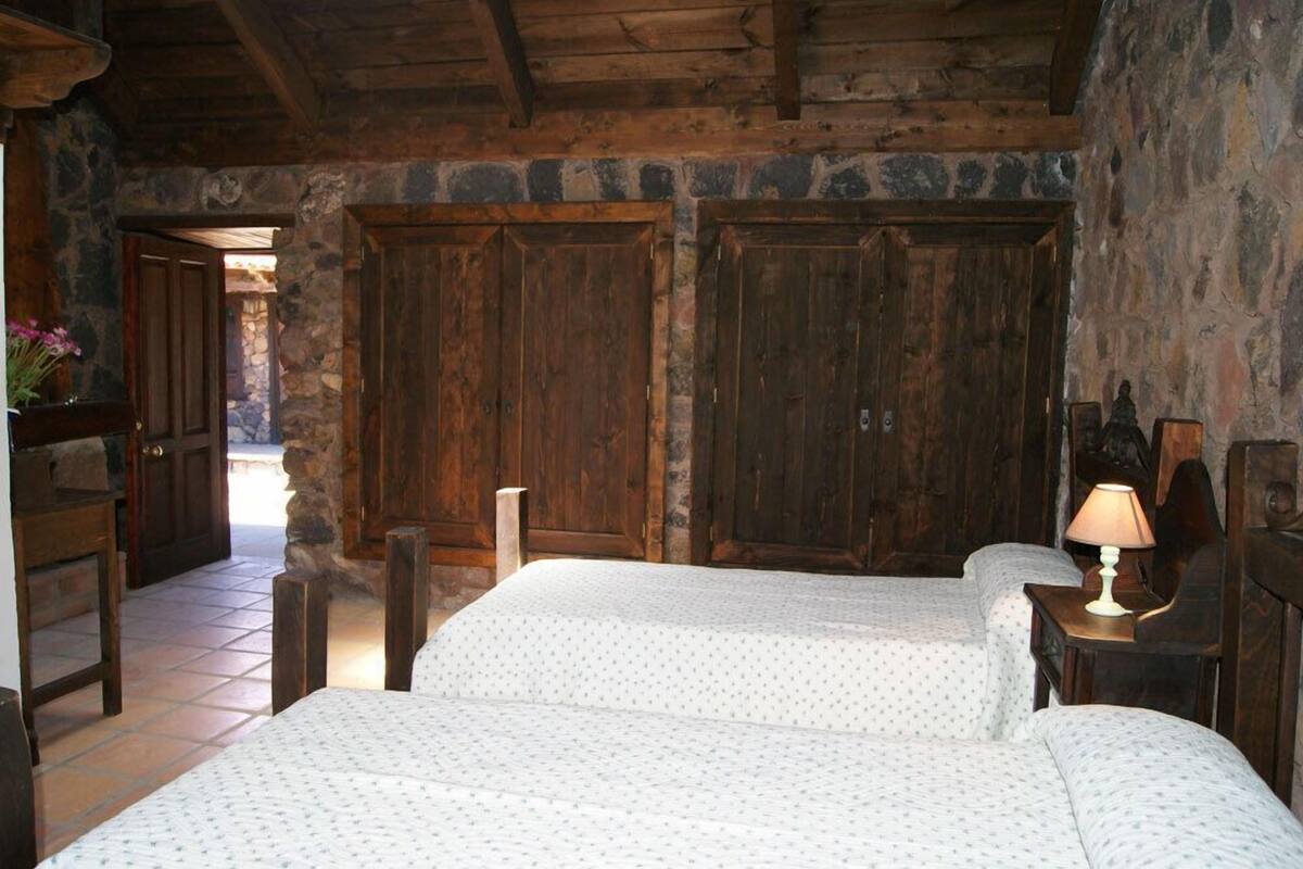 A rustic room with two beds, wooden doors, stone walls, and a tiled floor.