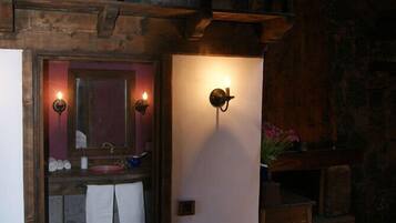 Un baño rústico con pared de piedra, vigas de madera, un lavabo con espejo y dos luces fijadas a la pared.