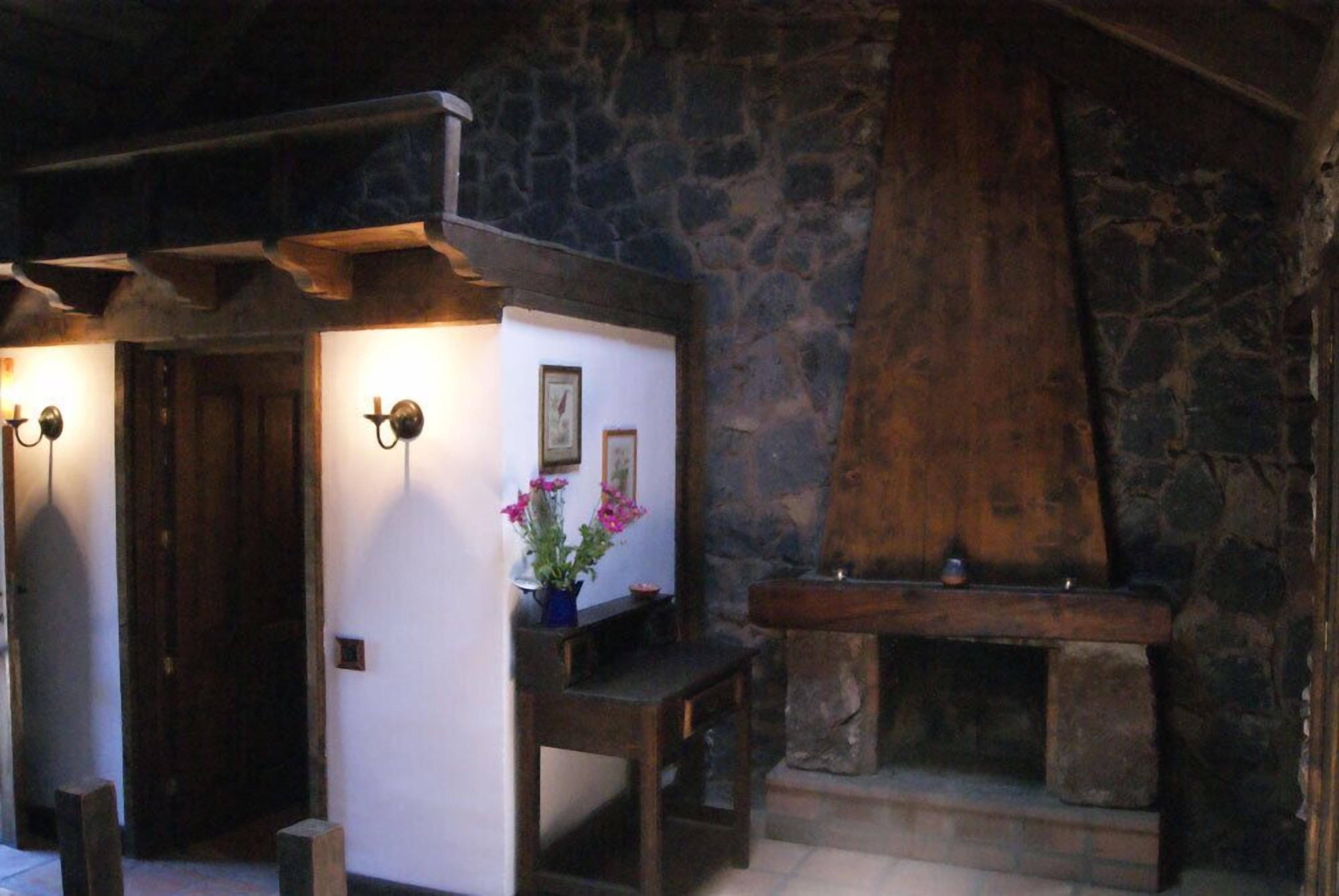 Ett rum med väggar av sten, en träbänk, ett litet bord med en vas med blommor och en öppen spis.