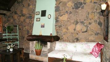 Una habitación acogedora con pared de piedra, un banco de madera, un sofá con cojines florales y una mesita con un jarrón.