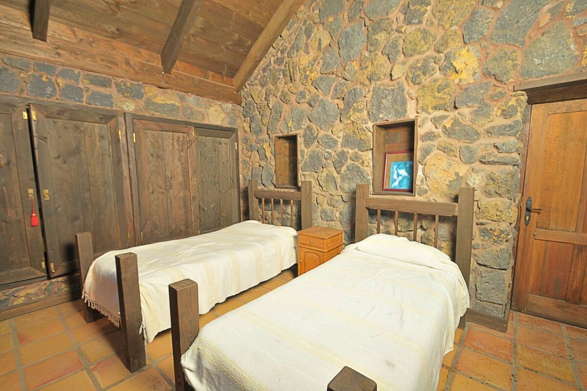 A rustic room with two wooden beds, stone walls, and wooden doors.