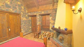 Una habitación acogedora con paredes de piedra, muebles de madera, chimenea y una colcha roja.