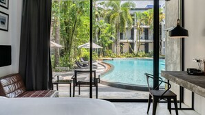 A hotel room with a large window, a bed, a desk, and a view of a swimming pool and tropical garden. - Kokotel Khao Lak Lighthouse (Takua Pa)