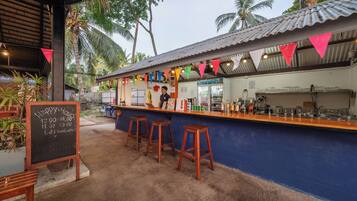 Zona de bar al aire libre con menú en pizarra, taburetes y una barra con varias botellas.