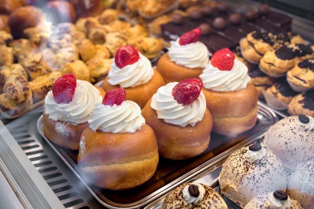 A display case with various pastries, including cream puffs topped with whipped cream and strawberries.