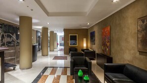 Un vestíbulo de hotel con piso de cuadros, sofás de cuero negro, una recepción y obras de arte en las paredes.