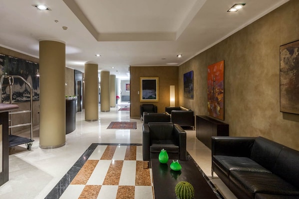 Eine Hotelhalle mit Schachbrettmuster-Boden, schwarzen Ledersofas, einem Empfangsbereich und Kunstwerken an den Wänden.