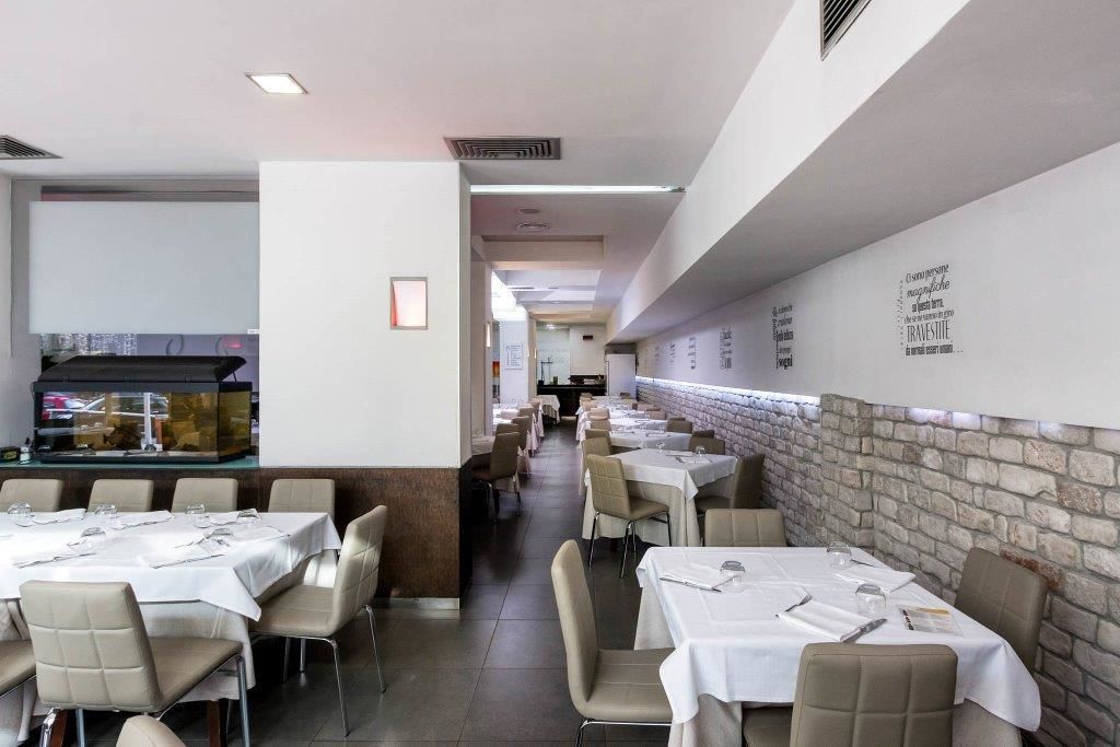 A restaurant with multiple tables and chairs, a counter with a display, and a brick wall with text.
