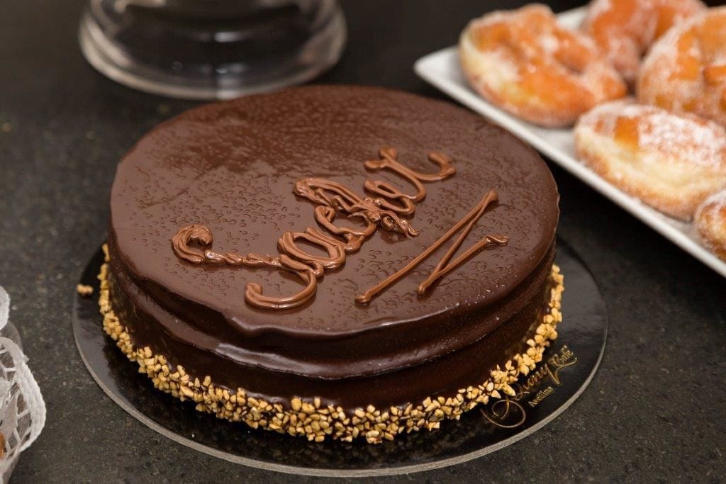 Un pastel de chocolate con la palabra 'SUGAR' escrita encima, rodeado de un borde de confites dorados.