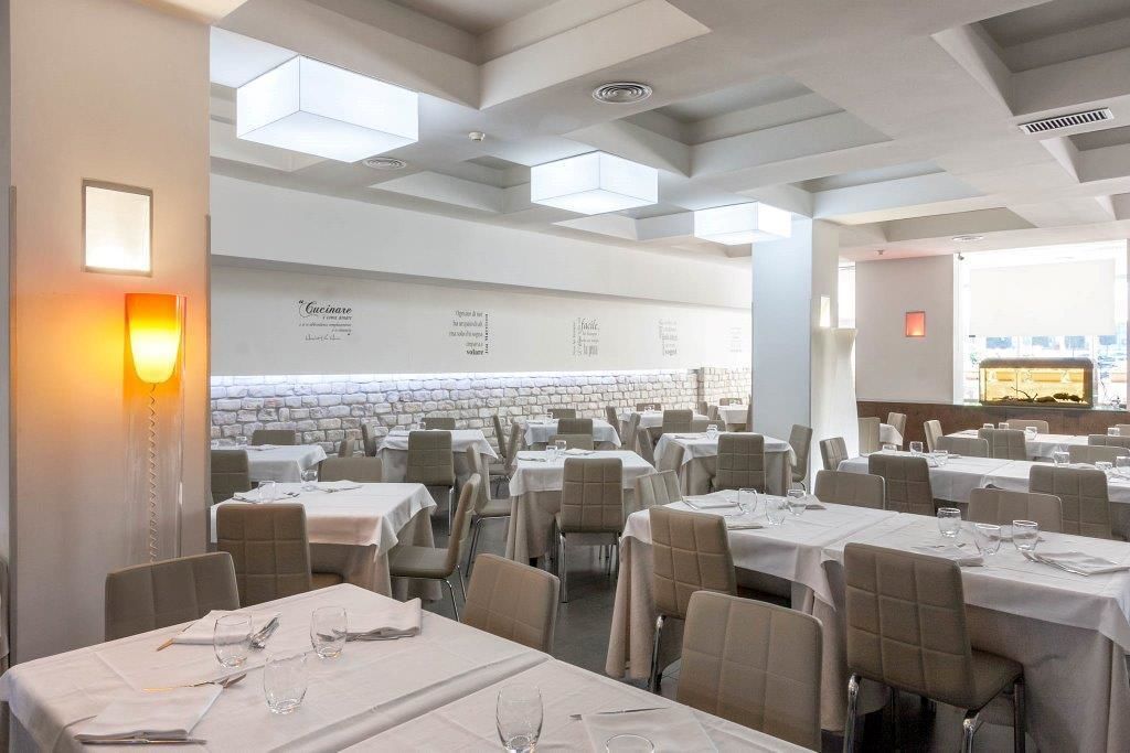A restaurant with multiple tables, each set with white tablecloths and chairs, and a stone wall in the background.