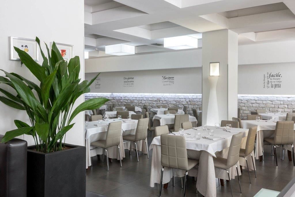 A restaurant with multiple tables and chairs, a potted plant, and a stone wall.
