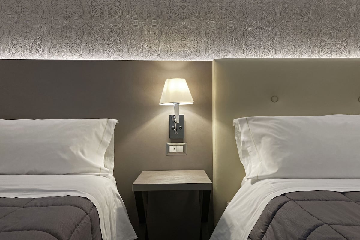 A hotel room with two beds, a nightstand with a lamp, and a patterned ceiling.