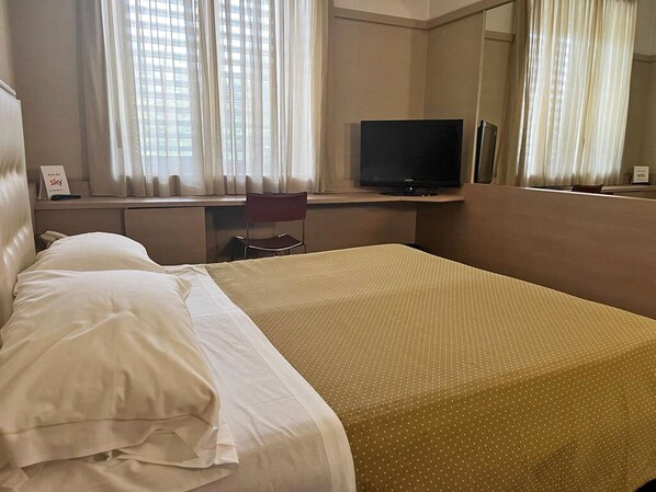 A hotel room with a bed, a desk with a television, and a chair.