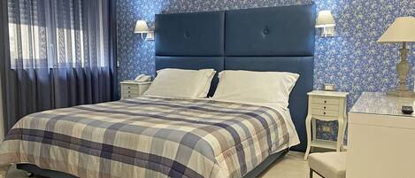 A neatly made bed with a checkered bedspread, a blue headboard, two bedside tables with lamps, and a patterned wallpaper.