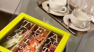 A glass table with a tray holding two white cups and saucers. In front of the table is a yellow-framed box with the text "TEA, ELLEN GIMNET, SUGAR" visible.