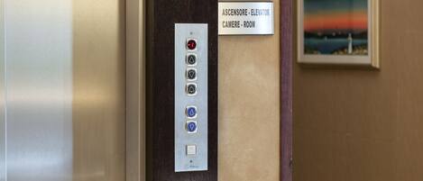 An elevator control panel with floor selection buttons and a sign indicating "Ascensore - Elevator" and "Camere - Room".