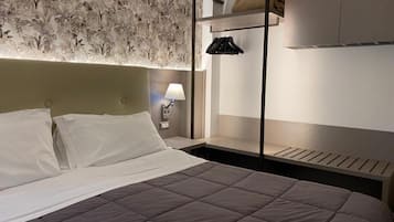 Ein modernes Hotelzimmer mit einem Bett, einem Nachttisch mit Lampe, einem Kleiderschrank und einem Kopfteil mit floralem Muster.