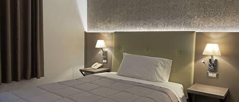Habitación de hotel con cama, dos mesitas de noche con lámparas, un teléfono y un cabecero estampado.