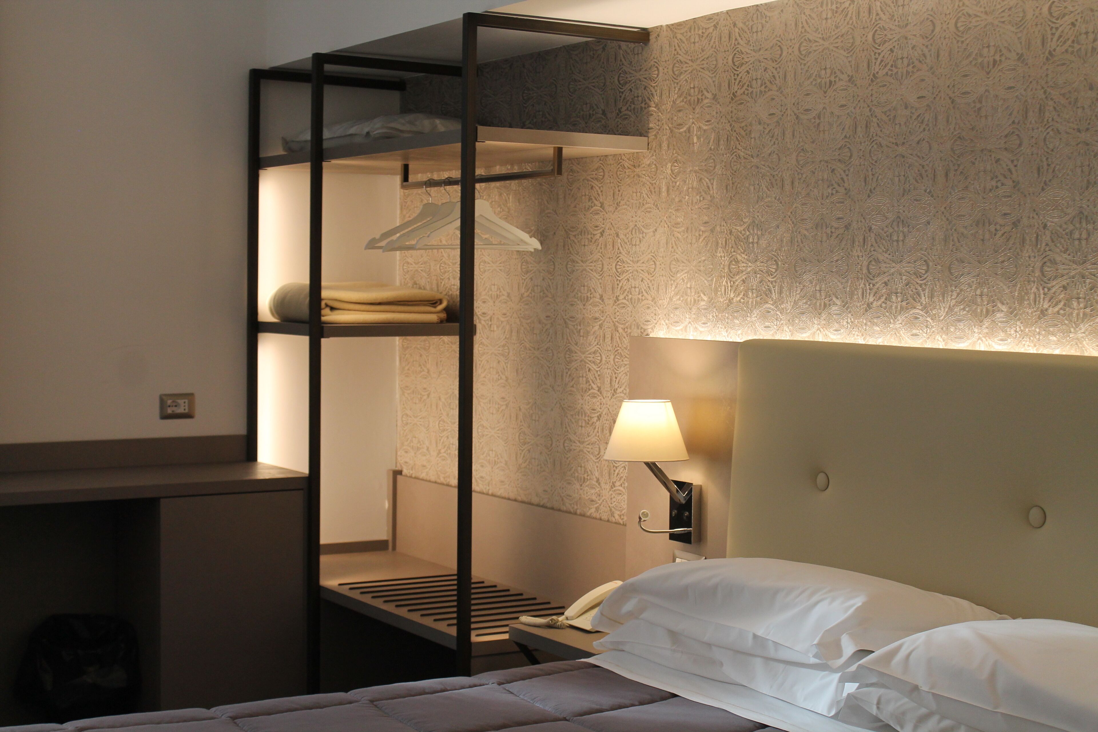 Una cama litera con un perchero, una mesita de noche con lámpara y un muro decorado.