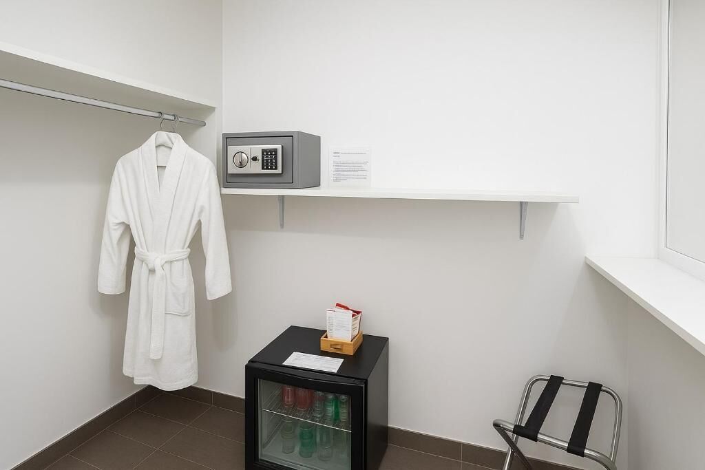 Un baño con una bata blanca colgada en un perchero, un mueble negro pequeño con puerta de cristal que contiene artículos de aseo, y un teclado de seguridad en un estante.