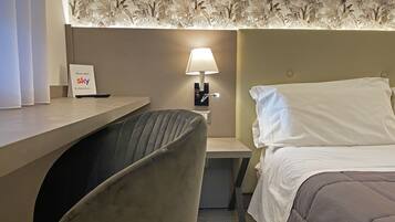 A hotel room with a bed, a desk, a chair, a lamp, and a sign indicating a Sky channel room.