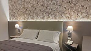 Una cama bien hecha con un edredón marrón oscuro, dos lámparas de noche y un papel tapiz estampado con flores.