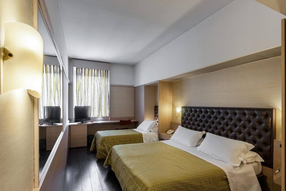 A hotel room with two beds, a desk, a chair, and a TV.