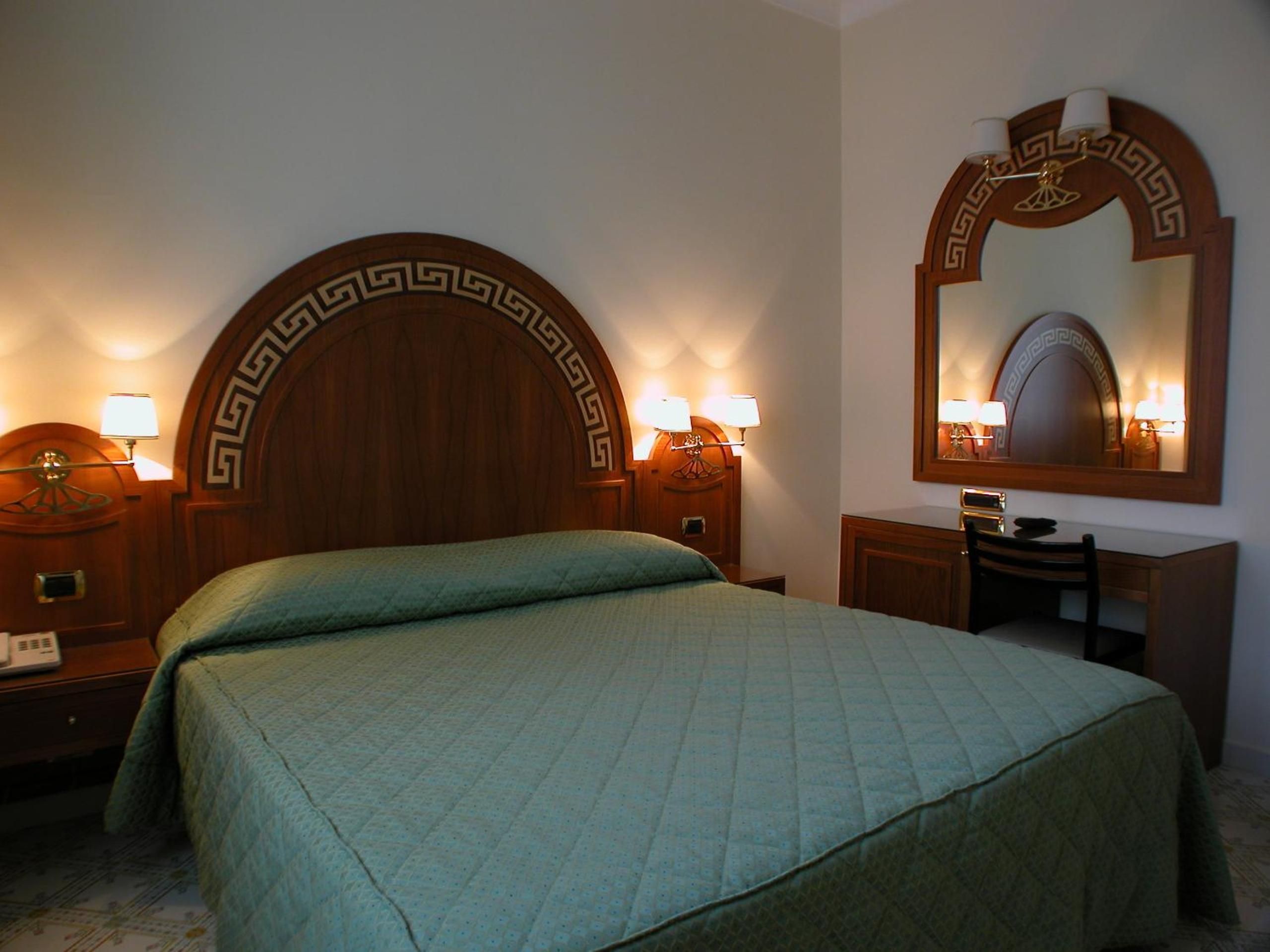 Habitación de hotel con una cama grande, un escritorio con silla, un espejo y dos lámparas de noche.