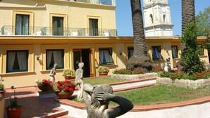A building with a yellow facade, a bell tower, and palm trees.