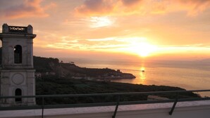 A coastal sunset view with a bell tower and a balcony railing.
